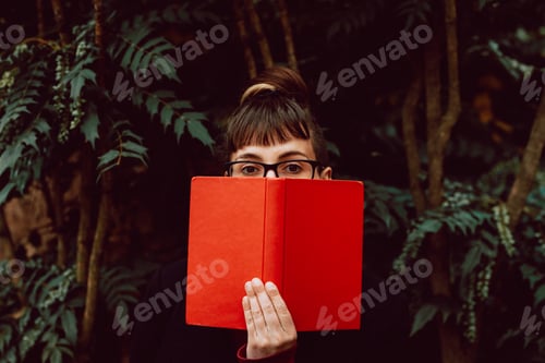 Preview: Young woman reading book on bench in park