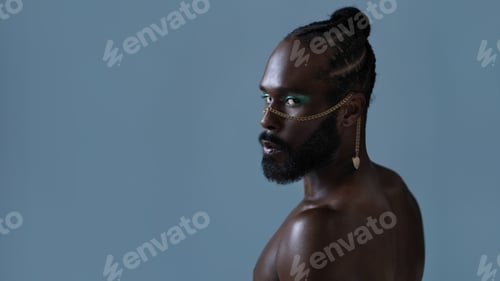 Preview: Serious black gay man with light makeup and gold accessory on face