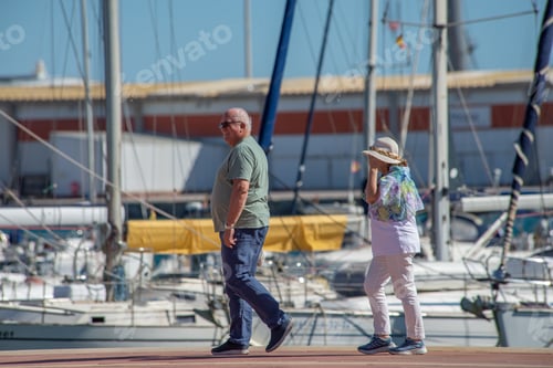Preview: Elderly couple walking along pier surrounded by boats, yachts with masts.