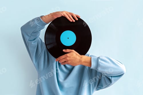 Preview: Man in blue sweatshirt covers his face with vinyl record on blue background