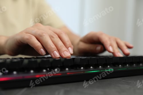 Preview: Woman typing on black keyboard with RGB lighting at grey table, closeup