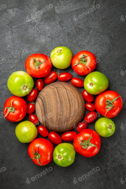 Preview: top view cherry red and green tomatoes around a wooden plate on dark ground with free space
