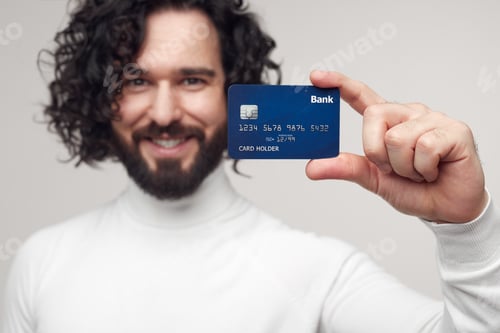 Preview: Smiling man showing credit card in hand in studio