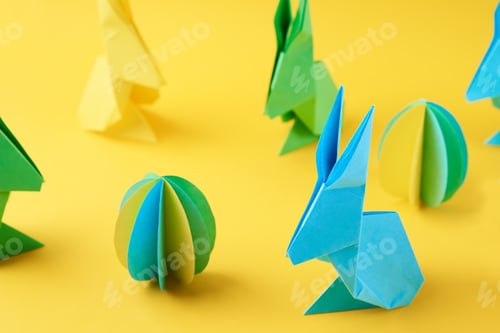Preview: Paper origami Esater rabbits and colored eggs on yellow background. Easter celebration concept