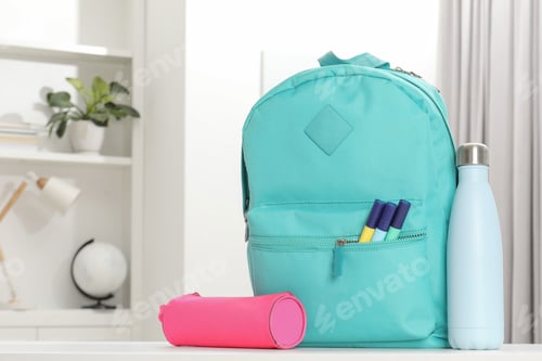 Backpack with different school stationery and bottle on desk in room