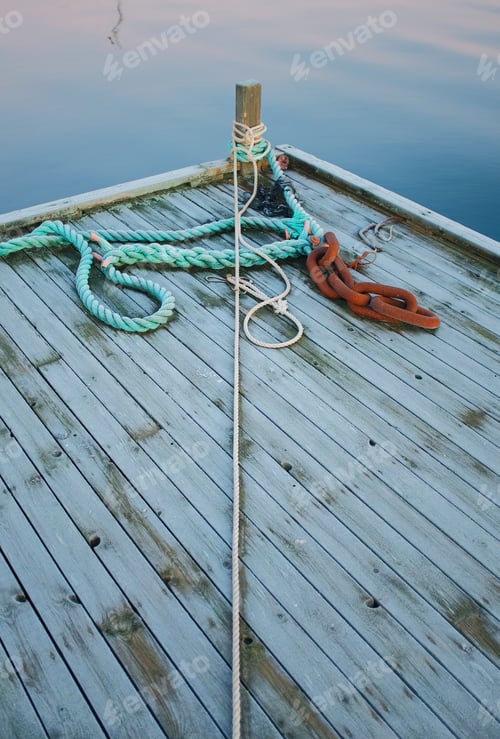 Preview: empty wooden pier with a ropes and a reflection of a ship on a surface of a sea in the background