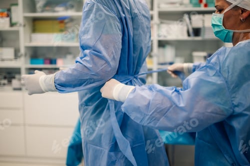 Preview: Medical professional ties surgeon's gown for surgery in sterile room.