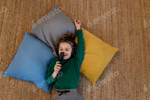 Preview: Little girl lying on the floor on cushions listening music,singing having fun and playing at home.