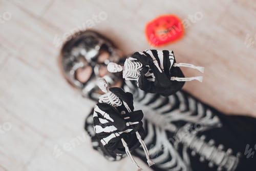 Preview: A boy in a Halloween skeleton costume lies on the floor and holds skeletons in his hands.