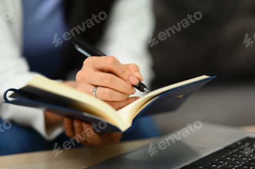 Preview: Cropped shot of woman hand writing notes in personal daily planner, planning workday