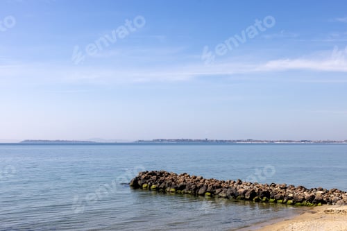 Preview: Rocky breakwater by calm sea with distant coastline in Burgas, Bulgaria.