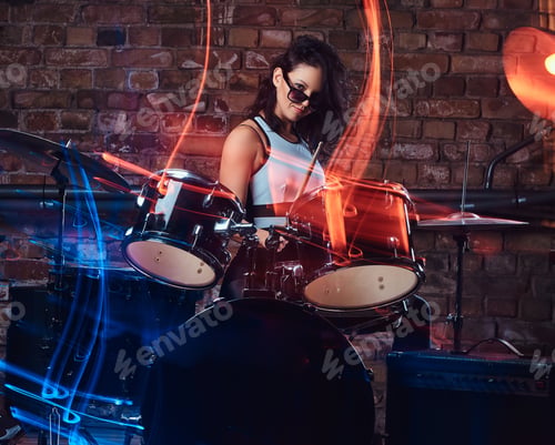 Preview: Beautiful girl musician in sunglasses holding the sticks sitting behind the drum set