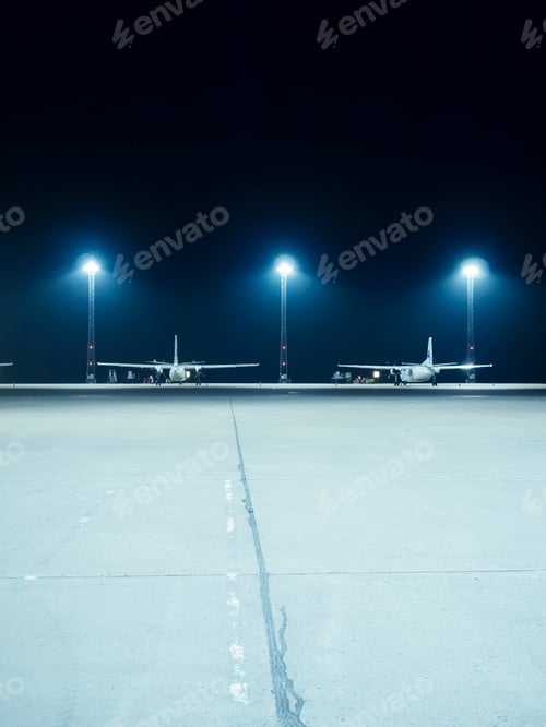Preview: Illuminated floodlights in front of airplanes parked at terminal
