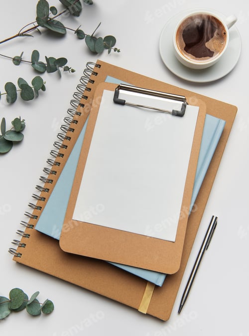 Preview: Clipboard with blank paper, notebooks and coffee cup on white table
