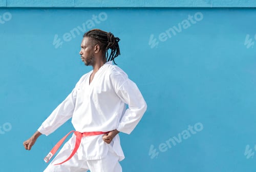 Preview: a young african american man training taekwondo outdoors on a blue background