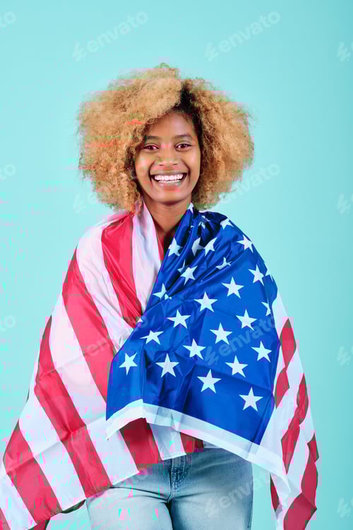 Preview: Young afro woman smiling while wrapped with an USA flag over an isolated background.
