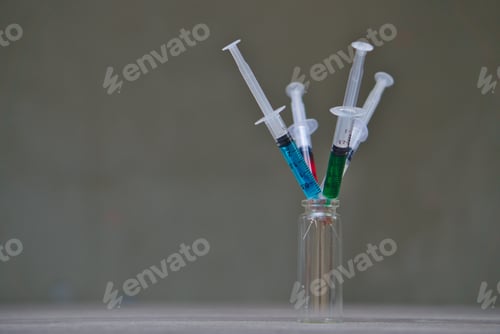 Preview: Closeup of syringes with colorful liquids in a vial against a gray background background.