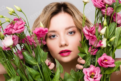Preview: beautiful spring young woman looking out from bouquet of Eustoma flowers isolated on grey