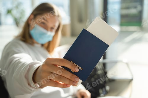 Preview: Young woman in a mask sits in an airport lounge during a pandemic and shows her passport