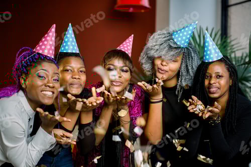 Visualização: Festa de confete. Feliz grupo africano jovem de pessoas celebrando a véspera de ano novo e soprando confetes