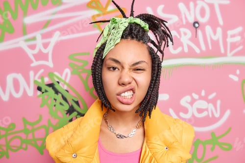Preview: Teenage lifestyle concept. Cheeky hipster girl with combed dreadlocks clenches teeth smirks face loo