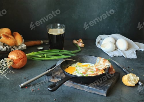 Preview: Fried eggs with bacon in a frying pan on the table, beer and other food products for lunch