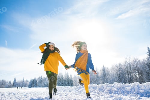 Preview: Young cheerful friends on a walk outdoors in snow in winter, running.