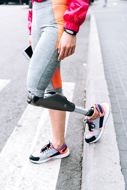 Preview: partial view of disabled sportswoman with prosthesis holding smartphone on street
