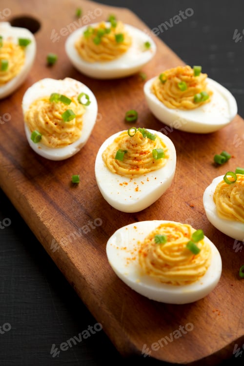 Preview: Homemade Deviled Eggs with Chives on a rustic wooden board on a black background, side view.