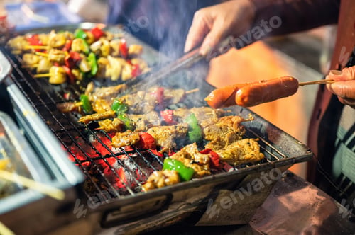 Preview: Seller using tongs grilling barbeque pork and sausage on charcoal stove