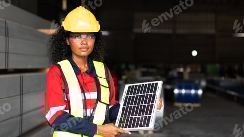 Preview: A industrial worker in a yellow helmet and safety vest holding a solar panel.