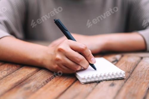Preview: Closeup image of a woman writing on blank notebook on wooden table