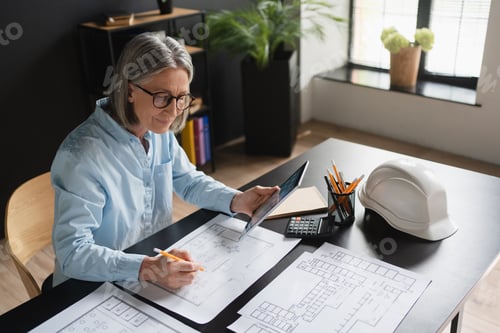 Preview: Caucasian female engineer architect using tools and electronic devices while drawing blueprints