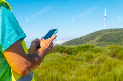 Preview: Hands of a woman worker in a wind farm, green energy, technical review, with the phone in her hand