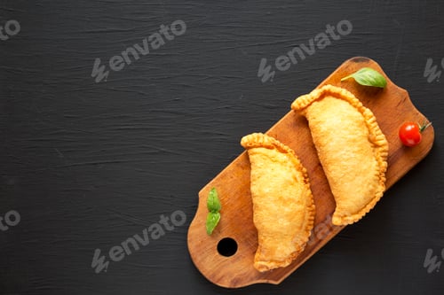 Preview: Homemade Deep Fried Italian Panzerotti Calzone on a rustic wooden board on a black background