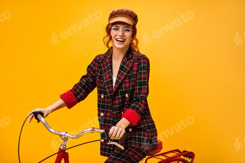 Preview: Pretty woman in stylish outfit rides bicycle on orange background. Modern girl with wavy hair in fa