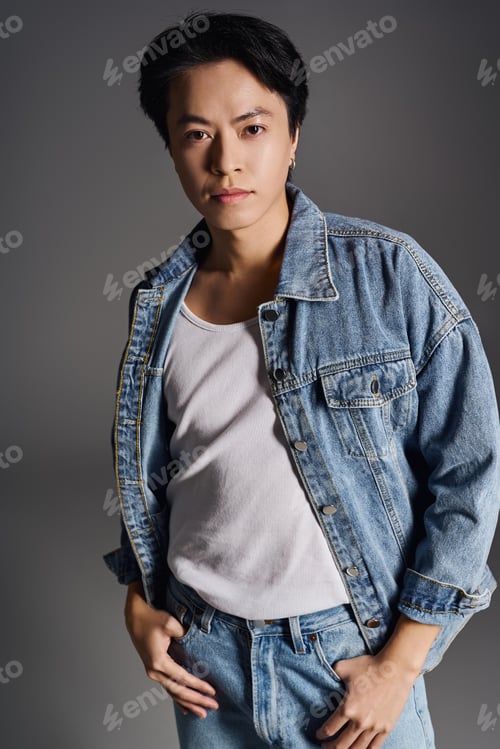 Preview: Young asian man showcases casual style in denim attire in a minimalist grey studio
