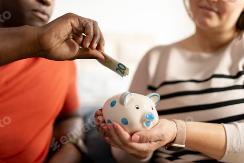 Preview: Close up view of couple hands putting money into a piggy bank