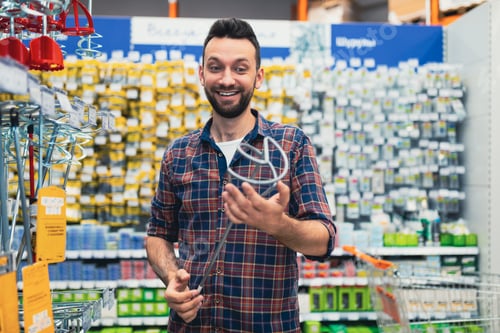 Preview: satisfied customer in a hardware store with a mixer attachment in his hands.