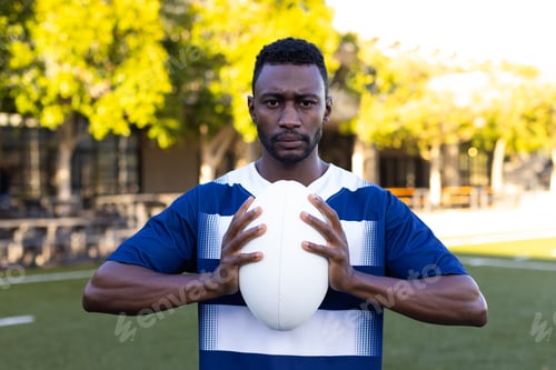 Preview: African American young male athlete holding a rugby ball on field outdoors, looking focused
