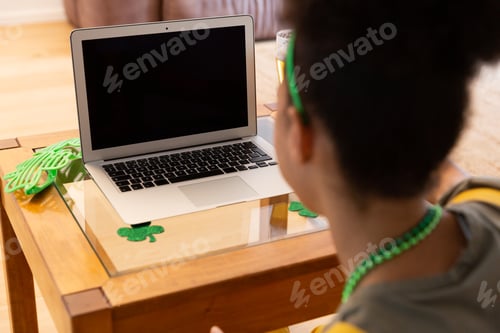 Preview: Mixed race woman celebrating st patrick's day making video call using laptop