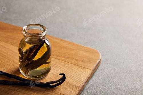 Preview: Vanilla pods and essential oil on wooden cutting board on dark surface
