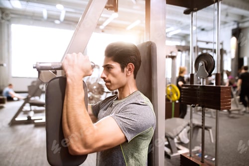 Preview: Hispanic man in gym sitting on bench, working out with weights