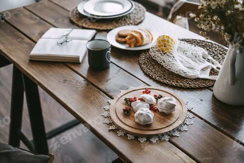 Preview: Wooden kitchen table with breakfast, book, cup of coffee and croissant.