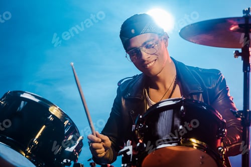 Preview: handsome mixed race male musician in leather jacket playing drums during rock concert on stage with