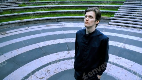 Preview: Tall man in black clothes standing in the meddle of amphitheater. Stock clip. Asphalt colored in