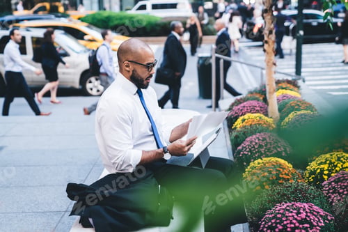 Preview: Ethnic man in business suit reading documents on street bench