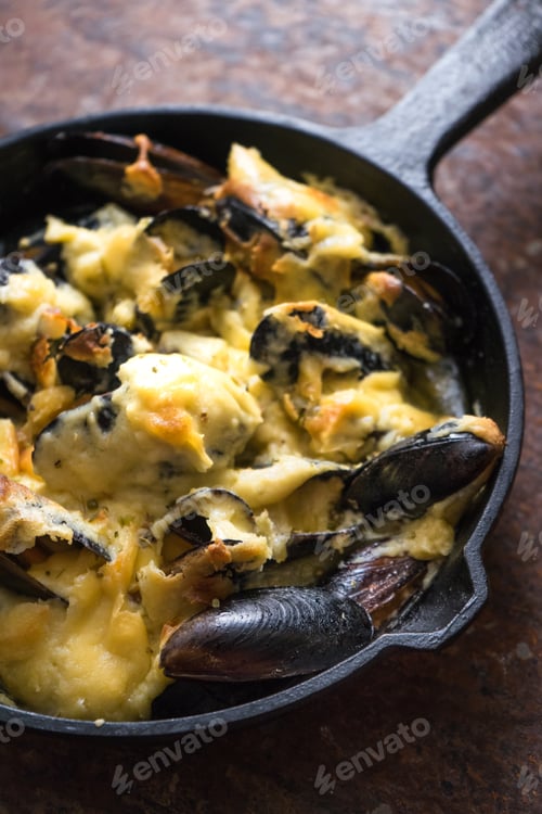 Preview: Frying pan with mussels under a cheese sauce on a brown background diagonal