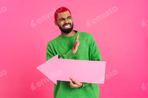 Preview: Displeased african american guy showing stop gesture and holding arrow placard