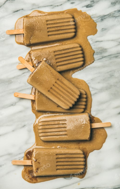 Preview: Flatlay of melting coffee latte popsicles over grey marble background